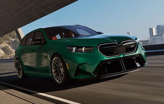 Green BMW M5 Touring driving on a city road. | Passport BMW in Suitland MD